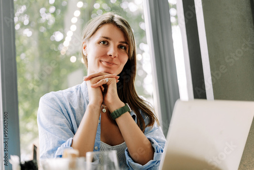 Smiling, attractive woman freelancer working on laptop in cafe looking at camera Free Download Smiling, attractive woman freelancer working on laptop in cafe looking at camera - GFXLoad