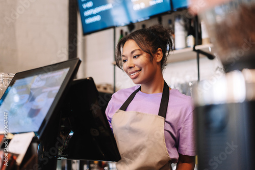 Young, smiling African American barista taking order on digital cash register photo