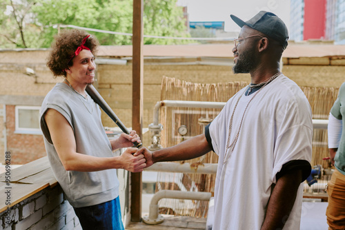 Curly haired man leaning on bricks while greeting his buddy in backyard photo