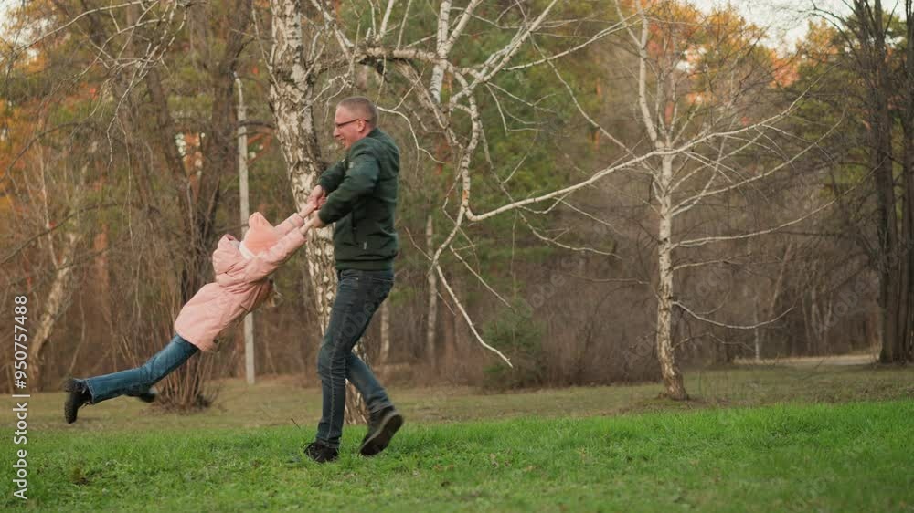 A man wearing a green jacket and blue jeans joyfully spins a little girl in a pink jacket on a green field in a park. pure joy and energy of a playful moment between a father and daughter A man wearing a green jacket and blue jeans joyfully spins a little girl in a pink jacket on a green field in a park. pure joy and energy of a playful moment between a father and daughter