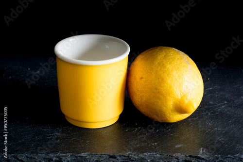 Lemon and yellow cup of coffee on black stone surface against a black background
