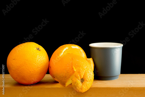 Orange fruit and a blue cup of coffee on a wooden shelf. Black background.
