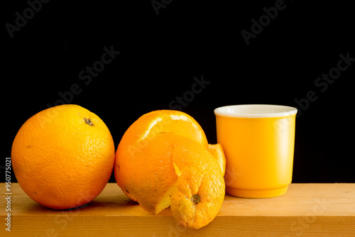 Orange fruit and a cup of coffee on a wooden shelf. Black background.