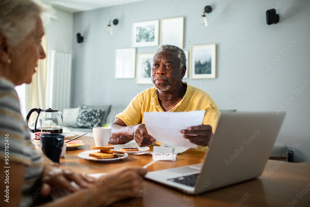 Diverse senior couple going over financials with laptop during breakfast Diverse senior couple going over financials with laptop during breakfast