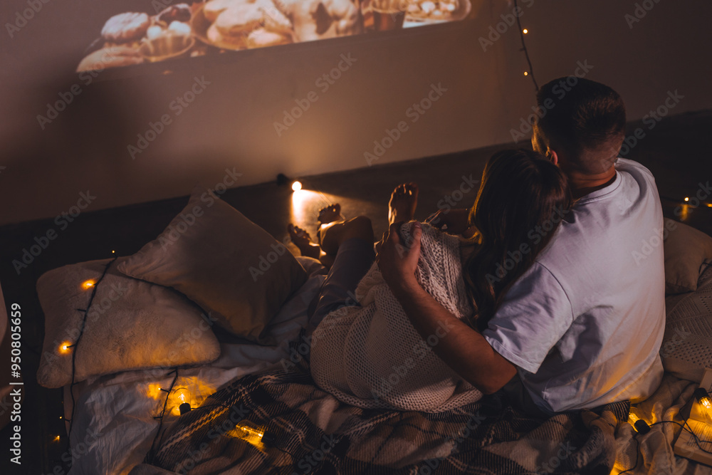 Obraz premium Romantic surprise for girlfriend or boyfriend. Bedroom prepared for watching old movies with popcorn, decorated with lights and candles. Cozy home Christmas atmosphere, hot chocolate with marshmallow