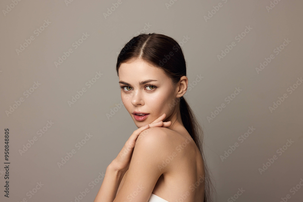 Beautiful young woman with long hair posing in front of a gray background, with her hands on her chin and looking at the camera Beautiful young woman with long hair posing in front of a gray background, with her hands on her chin and looking at the camera