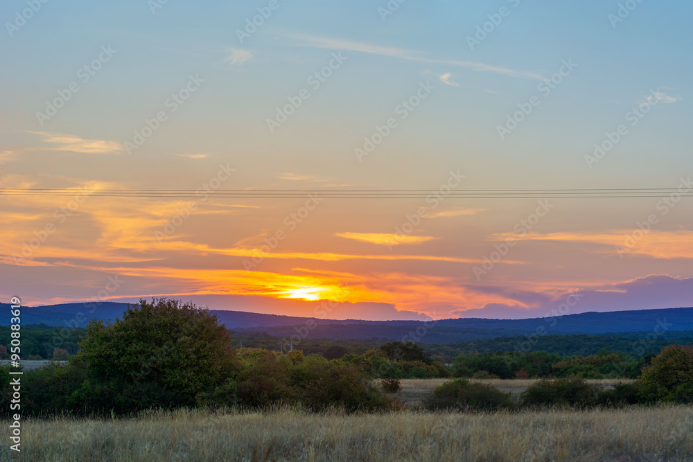 Sunrise or sunset against a blue cloudy sky. Clouds are highlighted with orange. Rich colors. Travel, peace and tranquility. The sun has disappeared behind the horizon. Mountains, forest and trees Sunrise or sunset against a blue cloudy sky. Clouds are highlighted with orange. Rich colors. Travel, peace and tranquility. The sun has disappeared behind the horizon. Mountains, forest and trees