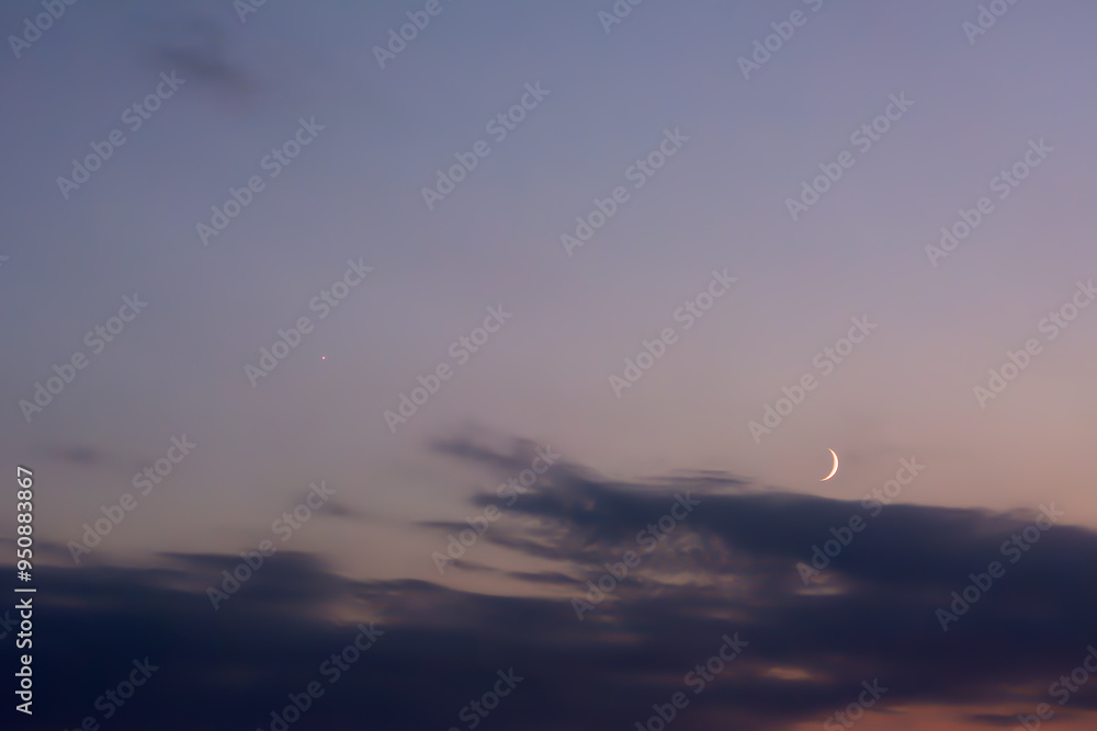 New moon rising above the horizon against a cloudy sky. Blue, grey and yellow colours. Astronomy, observing stars and earth satellites. New moon rising above the horizon against a cloudy sky. Blue, grey and yellow colours. Astronomy, observing stars and earth satellites.