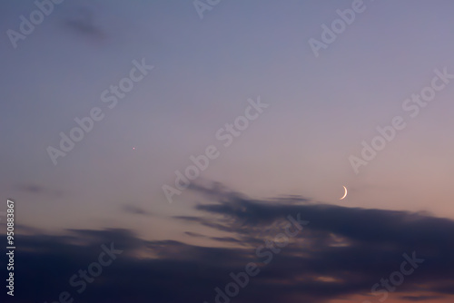 New moon rising above the horizon against a cloudy sky. Blue, grey and yellow colours. Astronomy, observing stars and earth satellites.