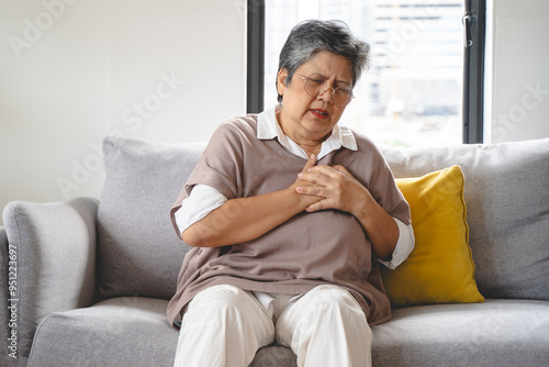 Asian elderly grabbing her chest and feeling pain from heart attack suddenly at home.