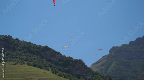 Paragliders Mountains Sky - Several paragliders fly over mountain peaks under a blue sky.