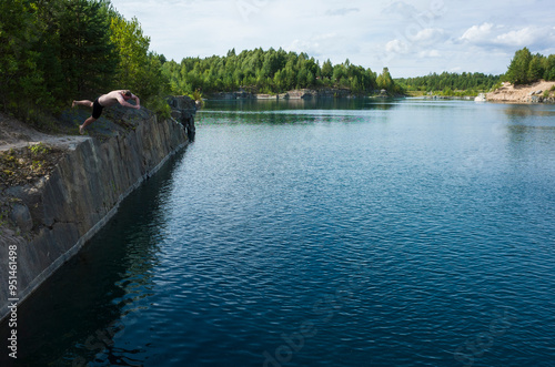 Adult man diving from rocky cliff in to blue water of flooded old quarry surrauded by forest on summer day, In central Sweden near Romfartuna photo