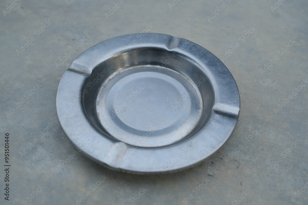 Closeup of a silver metal ashtray on a concrete surface. Closeup of a silver metal ashtray on a concrete surface.