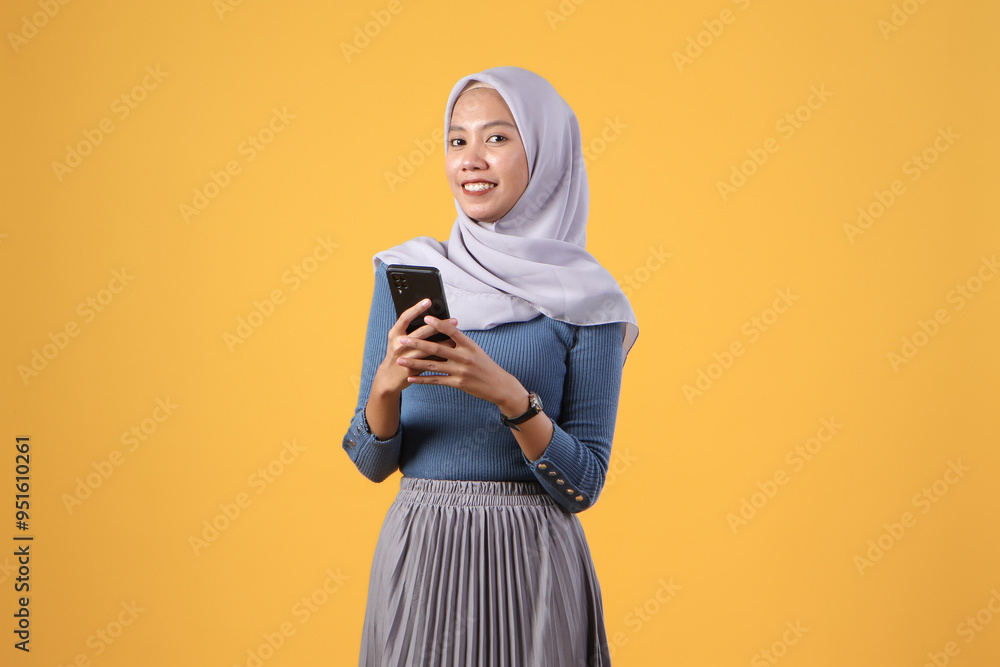 asian indonesian muslim woman holding smart phone giving thumb up finger gesture on isolated yellow background asian indonesian muslim woman holding smart phone giving thumb up finger gesture on isolated yellow background