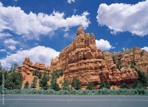 Utah, USA - July 1, 2006: Summer view of asphalt road against red sedmentary rock cliffs with the background of cumulus in the blue sky photo