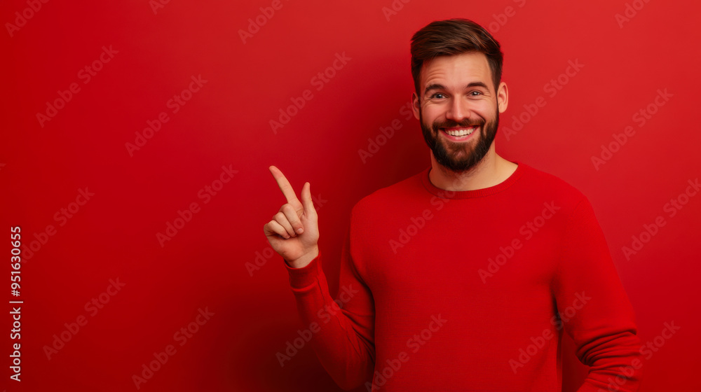 A cheerful man in a red sweater smiles and points to the side against a vibrant red background in a well-lit indoor setting A cheerful man in a red sweater smiles and points to the side against a vibrant red background in a well-lit indoor setting