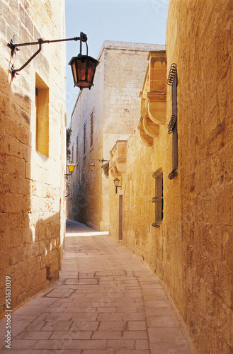 Mdina, Malta - July 1, 2008: Summer view of a street lamp on the stone wall of a house with narrow curved alley