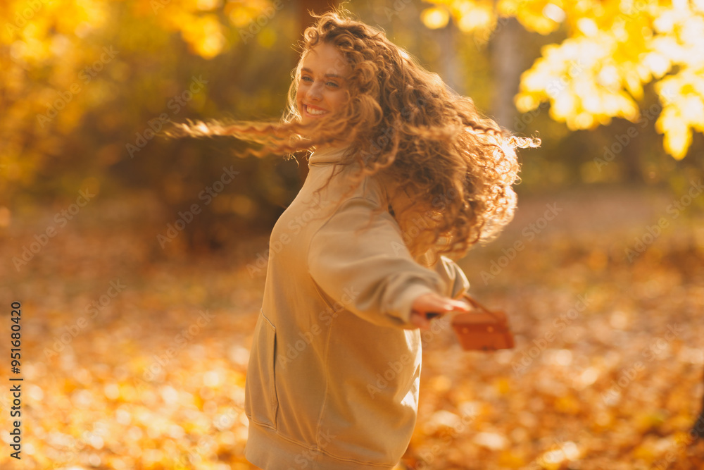 Naklejka premium Smiling young woman enjoys the autumn weather in the forest with the yellow leaves at sunset