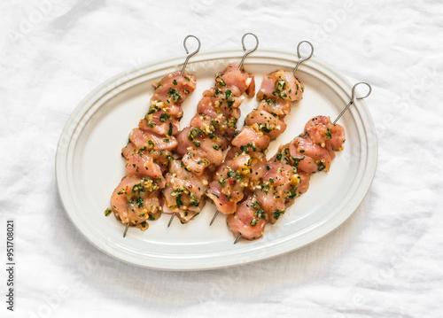 Raw marinated chicken skewers on an oval plate on a light surface