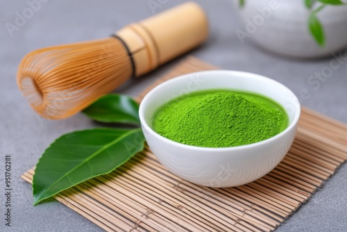 A White Bowl of Matcha Tea with a Leaf and Wooden Whisk on a Bamboo Mat