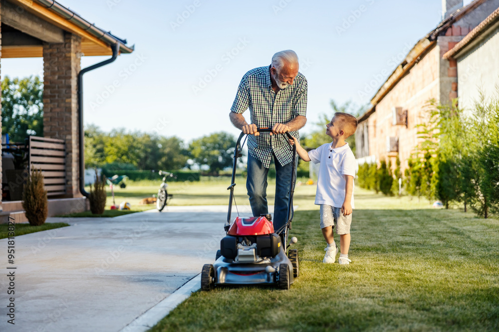 Front view of granddad and grandson mowing lawn in backyard together. Front view of granddad and grandson mowing lawn in backyard together.