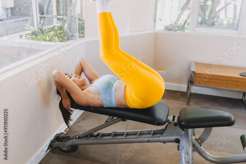 Asian woman in yellow blue fitness outfits do Lying Bench Leg Raise in he gym. photo