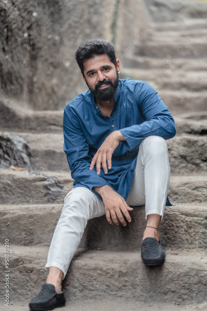 handsome indian bearded black hair man wearing traditional clothes blue kurta. sitting on stone steps smiling handsome indian bearded black hair man wearing traditional clothes blue kurta. sitting on stone steps smiling