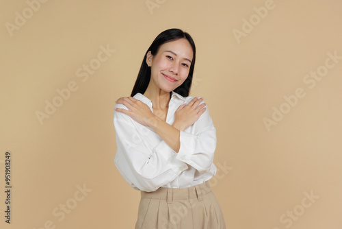 Smiling Woman Hugging Herself in a Warm Gesture, Beige Background