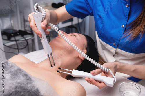 Young middle-aged Caucasian woman receiving electrical stimulation. Electrical facelift at a professional cosmetologist appointment