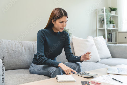 young woman looking at credit card invoice checking receipt before pay debt via mobile app at home