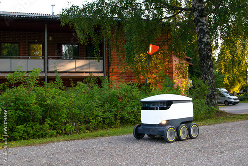 A delivery robot on wheels completes a home delivery from the grocery store. The self-driving courier navigates traffic on the road. Efficient shipping ensures quick takeaway service. photo