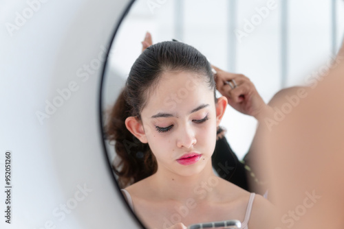 Teenage girl looks into the smartphone while her mother combs her daughter's hair