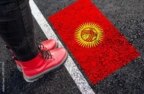 a woman with a boots standing on asphalt next to flag of Kyrgyzstanl and border