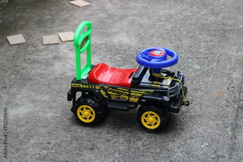 Colorful toy jeep with yellow wheels on a grey concrete surface.