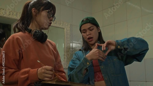 Medium shot of Caucasian and Asian ladies from film college planning interior of movie set using storyboard in washroom