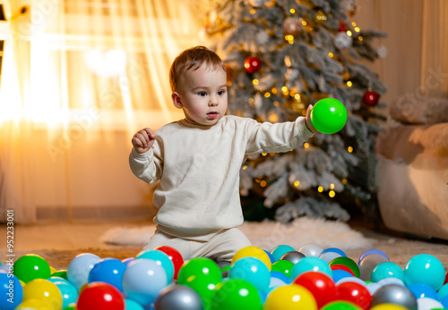 Toddler playing with colorful balls in a cozy winter room. A young child enjoys playing with vibrant plastic balls, surrounded by festive decorations
