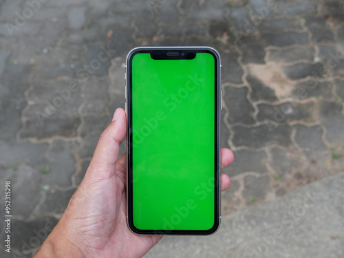 Green screen Smart phone screen, Hand-held smartphone with green screen, ideal for digital mockups, against a blurred background.