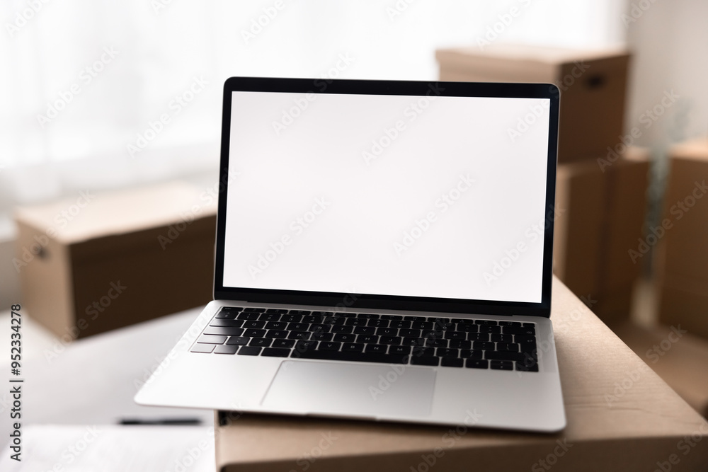 Close up laptop with white mock up on screen, placed on top of big cardboard box. Transportation services for relocation day, logistics, inventory management, electronic commerce marketplace platform Close up laptop with white mock up on screen, placed on top of big cardboard box. Transportation services for relocation day, logistics, inventory management, electronic commerce marketplace platform