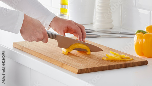 Closeup of a person slicing orange peppers on a wooden cutting board.