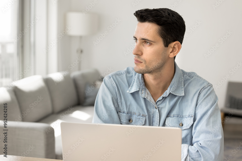 Serious pensive young Latin freelance entrepreneur man working at laptop at home, looking away in deep thoughts, thinking on solutions for business project, problem solving strategy Serious pensive young Latin freelance entrepreneur man working at laptop at home, looking away in deep thoughts, thinking on solutions for business project, problem solving strategy