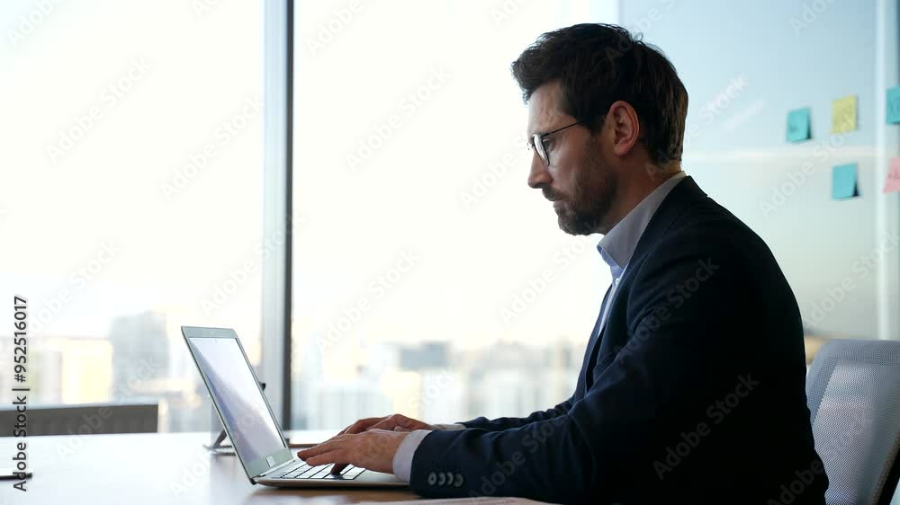 Male professional deep in thought working on laptop in office. Focused entrepreneur planning strategy in workplace, business growth. Atmosphere of focus, innovation. Silhouette on background of window Male professional deep in thought working on laptop in office. Focused entrepreneur planning strategy in workplace, business growth. Atmosphere of focus, innovation. Silhouette on background of window