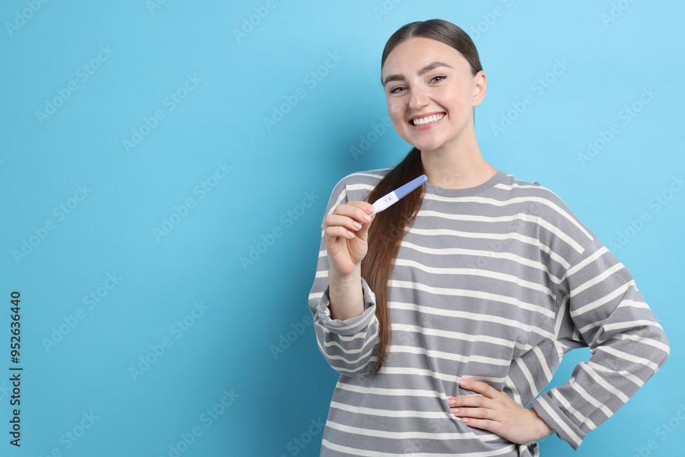 Happy woman holding pregnancy test on light blue background, space for text Happy woman holding pregnancy test on light blue background, space for text