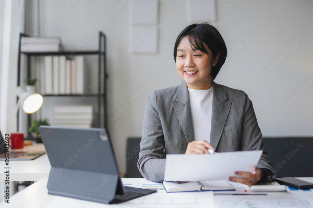 Young asian businesswoman smiling and having video call on tablet while reviewing paperwork and working at desk in modern office Young asian businesswoman smiling and having video call on tablet while reviewing paperwork and working at desk in modern office