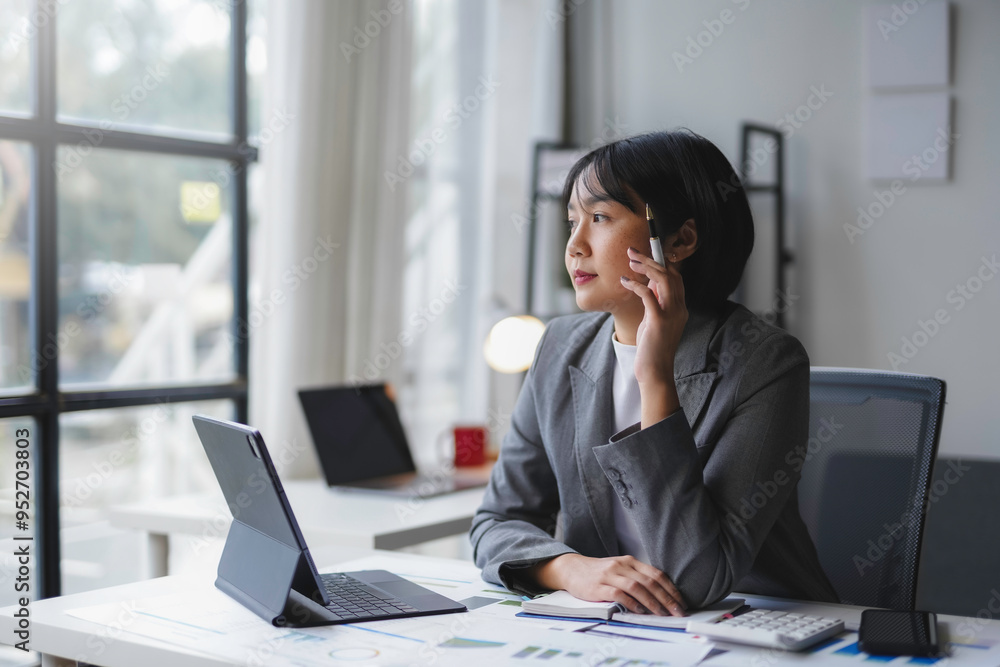Businesswoman is holding a pen and thinking about new business strategies while working on a tablet in the office Businesswoman is holding a pen and thinking about new business strategies while working on a tablet in the office