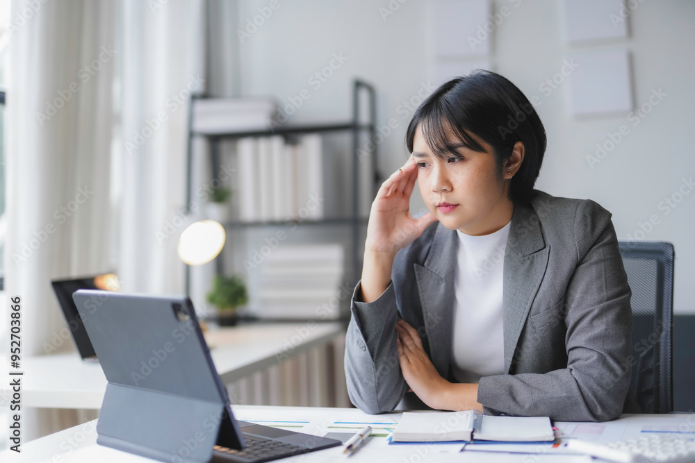 Stressed businesswoman touching her head with hand while working on laptop computer at office desk Stressed businesswoman touching her head with hand while working on laptop computer at office desk