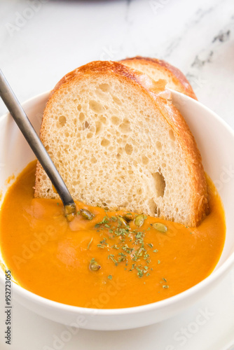 Bread slice dipped in butternut squash soup with herbs