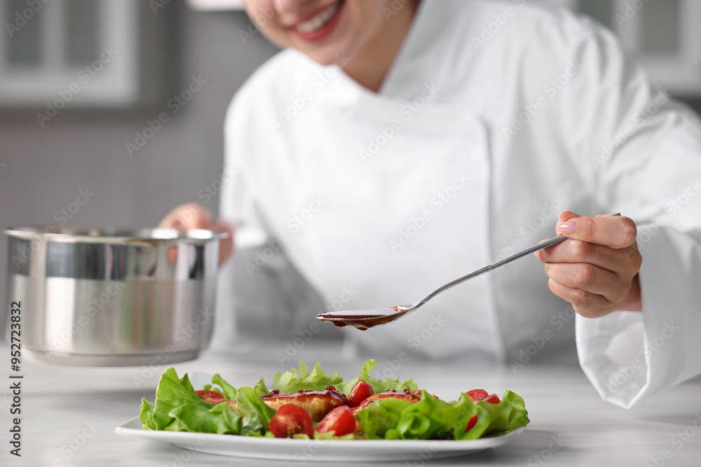 Naklejka premium Professional chef adding sauce to dish with baked chicken at white marble table in kitchen, closeup
