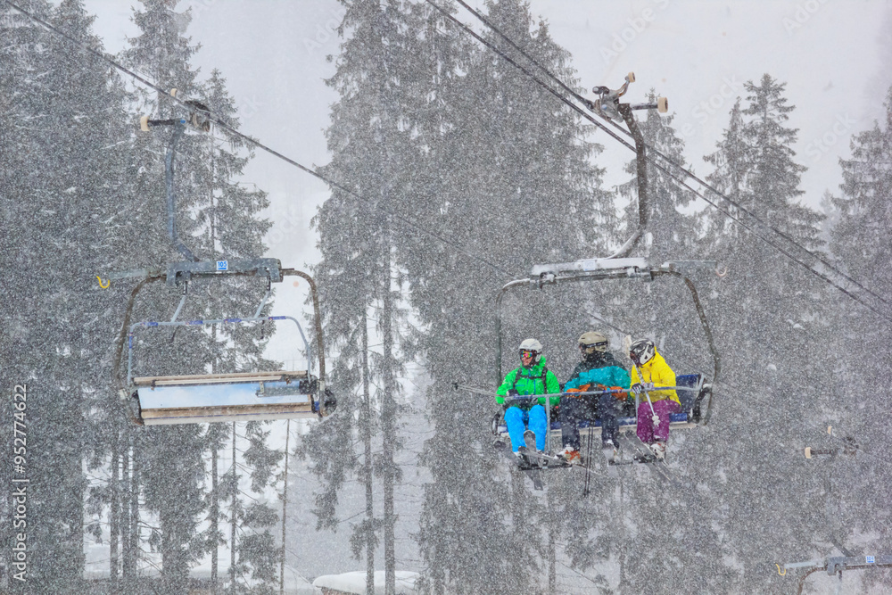Winter landscape - view of the chairlift lift with skiers in the winter mountain forest during a snowfall, Bukovel ski resort, Carpathian mountains, Ukraine