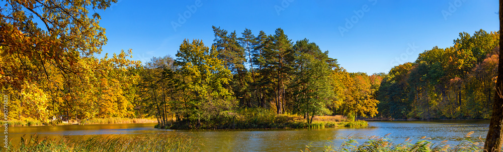 Fototapeta premium Autumn landscape, panorama, banner - view of a small island on the lake with reflection in the water of autumn trees against a clear blue sky