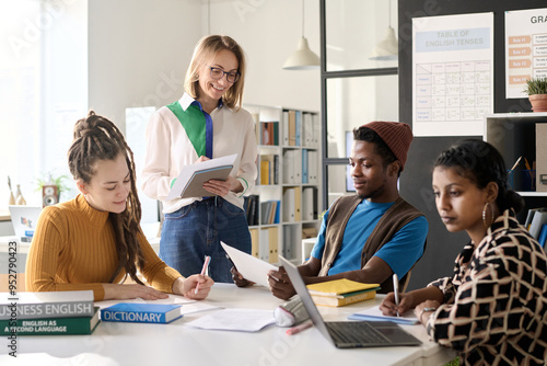 Portrait of female teacher working in class with group of college students sitting at table with computers photo